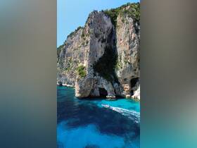 A scenic aerial view of a boat navigating through crystal-clear waters near stunning coastal cliffs, showcasing the beauty of the landscape and the adventure of exploring hidden coves.