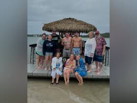 A cheerful group gathers at a dock for a birthday celebration, enjoying the company of friends and a dog in the water — a perfect moment for fun and memories.