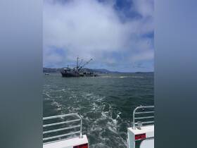 A fishing boat is seen working in the water, surrounded by scenic views of the coastline and hills, capturing the essence of maritime activities.