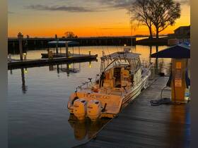 A serene sunset view of a boat named 'HERE WE GO' docked peacefully, reflecting the vibrant colors of the sky on the water's surface.