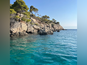 A stunning view of a rocky coastline with lush greenery and crystal-clear turquoise waters, perfect for exploring the beauty of nature while boating.