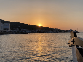 A serene sunset view over the coastline, captured from the deck of a boat, showcasing the tranquil waters and distant hills.