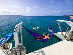Two friends enjoy a sunny day on the water, with one relaxing in a hammock and the other swimming nearby — a perfect scene for summer fun and relaxation.