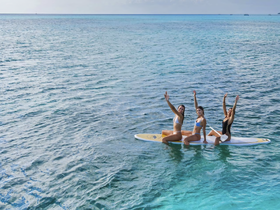 Three friends enjoy paddleboarding in crystal-clear waters, capturing a moment of fun and adventure under the sun.