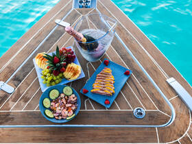 An exquisite display of gourmet food and drinks on a boat, featuring fresh shrimp, vibrant fruits, and a bottle of champagne, perfect for a luxurious day on the water.