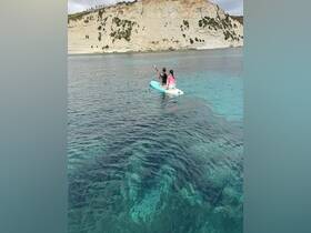 A couple enjoys paddleboarding in clear turquoise waters, surrounded by stunning coastal cliffs — a perfect adventure for water enthusiasts.