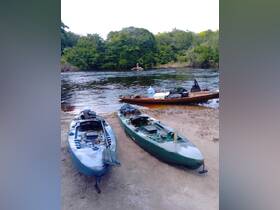 Two kayaks are docked on the sandy shore of a serene river, surrounded by lush greenery — perfect for a day of exploration and adventure in nature.