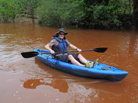 A man enjoys kayaking in a serene, muddy river surrounded by lush greenery, perfect for outdoor adventures and exploring nature.