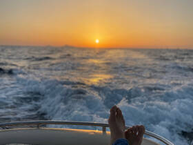 A serene sunset view from a boat, featuring a pair of feet resting on the edge, capturing the essence of relaxation on the water.