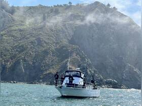 A fishing boat navigates near a rocky coastline, with crew members enjoying the scenic view — a perfect day for ocean adventures.