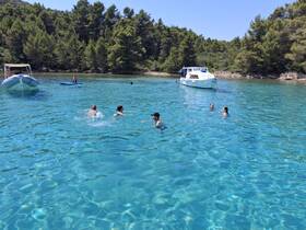 A lively group enjoys a refreshing swim in crystal-clear waters, with a boat anchored nearby, perfect for a fun day at the beach.