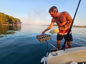 A man grills seafood on a boat while enjoying the serene waters and beautiful sunset — a perfect moment for culinary adventures on the water.