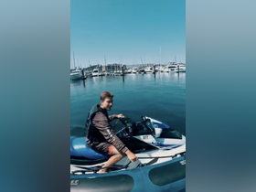 A young man enjoys a thrilling ride on a jet ski at the marina, surrounded by a fleet of boats — perfect for water sports enthusiasts.