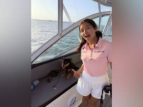 A young girl joyfully poses with her dog aboard a boat, capturing a fun moment on the water.