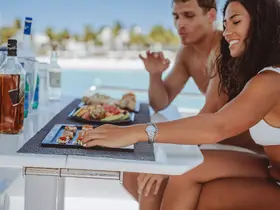 A couple enjoys a delicious spread of sushi and drinks aboard a boat, perfect for a relaxing day on the water.
