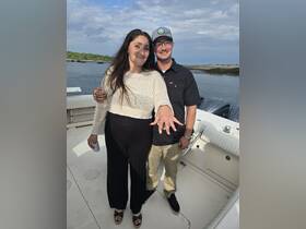 A couple celebrates their engagement on a boat, showcasing the ring and enjoying a beautiful day on the water.