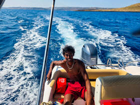 A young man enjoys a sunny day on the water, relaxing on a boat while cruising through beautiful ocean waves — a perfect moment for adventure and fun.