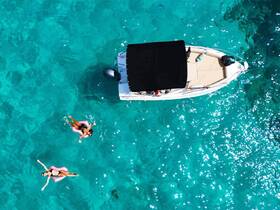Two friends enjoy a refreshing swim in crystal-clear waters while floating near a boat, capturing the essence of a perfect day on the water.