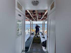 Inside view of a boat cabin showing a person preparing equipment, with seating and safety gear visible — a glimpse into the operational space of a fishing or tour vessel.