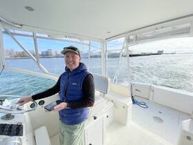 A smiling man stands at the helm of a boat, showcasing the interior cabin and control console, perfect for navigating the waters.