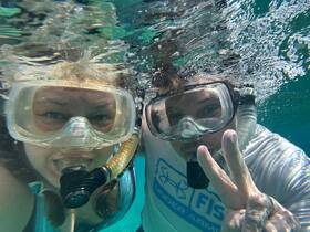 A couple enjoys snorkeling underwater, capturing a fun moment with smiles and peace signs — a perfect snapshot of aquatic adventure.