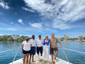 A cheerful group poses on the deck of a boat with a scenic waterfront backdrop, capturing a memorable moment on the water.