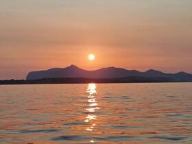 A stunning sunset casts a warm glow over the tranquil waters and distant mountains, creating a picturesque scene perfect for evening boat cruises.