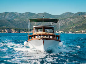 A classic boat glides through clear blue waters, showcasing its elegant design against a backdrop of lush mountains — perfect for scenic cruises.