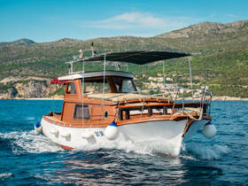 A classic yacht glides through clear waters, showcasing its elegant design against a scenic backdrop of hills and coastline.