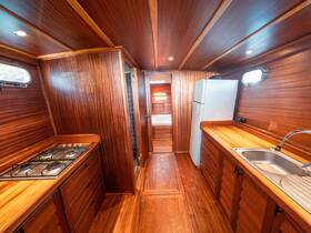 Interior view of a well-equipped boat kitchen featuring wooden cabinetry, a gas stove, and a refrigerator, perfect for onboard cooking and dining.