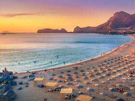 A stunning sunset view over a beach filled with umbrellas and people enjoying the water, showcasing the beautiful coastline and tranquil atmosphere.