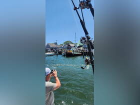 A fisherman captures the moment with his camera while enjoying a day on the water, surrounded by boats and a bustling waterfront scene.