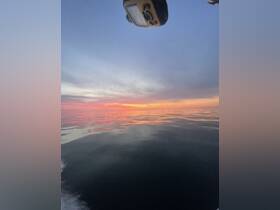 A partially obscured view of a sunset over calm waters, with an unclear angle and equipment visible in the frame.