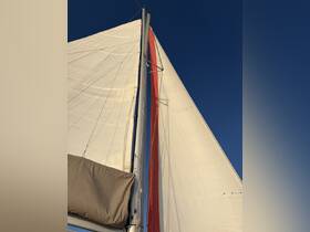 A close-up view of the sails and mast of a sailboat against a clear blue sky, showcasing the intricate rigging and vibrant colors of the sails.