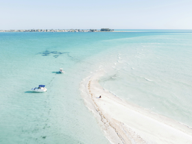 A stunning aerial view of boats anchored near a picturesque sandbar, showcasing the serene turquoise waters and beautiful coastline — an ideal spot for relaxation and exploration.