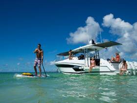 A group enjoys a sunny day on the water, with one person paddleboarding while others relax on the boat — a perfect scene for summer fun and water activities.