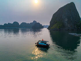 A serene aerial view of a boat navigating through tranquil waters, surrounded by stunning rock formations at sunset — a picturesque scene in nature.