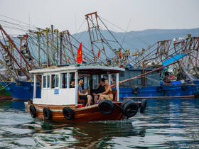 A group enjoys a leisurely ride on a small boat in a bustling harbor, surrounded by fishing vessels — a perfect snapshot of maritime life and camaraderie.