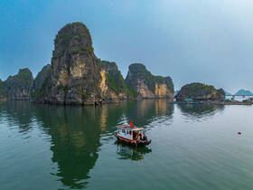 A serene view of a traditional boat navigating through the stunning limestone karsts of Ha Long Bay, showcasing the natural beauty and tranquility of this UNESCO World Heritage site.