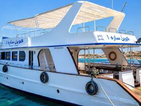 A stunning view of a yacht named 'كون سار 1' docked in clear waters, showcasing its elegant design and spacious upper deck, perfect for leisurely cruises.