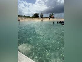 A scenic view of a beach with people walking along the shore and enjoying the clear waters — a perfect spot for a sandbar stop during a boating adventure.