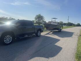 A boat is being towed by a pickup truck on a sunny day, showcasing the vessel's exterior while preparing for a day on the water.