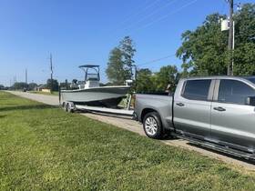 A boat is seen on a trailer, hitched to a pickup truck, parked alongside a grassy area on a sunny day — perfect for preparing for a day on the water.