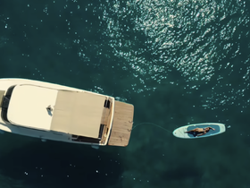 An aerial view captures a person relaxing on a paddleboard near a yacht, showcasing a perfect day on the water for sunbathing and leisure activities.