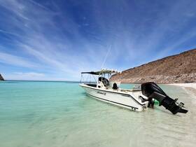 A sleek speedboat rests on the sandy shore, surrounded by crystal-clear waters and a stunning backdrop of rocky cliffs — perfect for a day of adventure on the water.