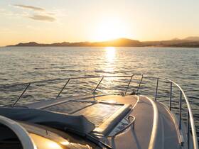 A serene sunset view from the bow of a yacht, showcasing the tranquil waters and distant hills — perfect for romantic evening cruises.