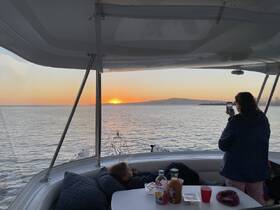A serene sunset view from a boat, with a woman capturing the moment on her phone while another guest relaxes nearby — perfect for memorable evening cruises.
