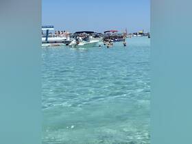 A lively scene at a popular beach spot with multiple boats and groups of people enjoying the water — perfect for summer fun and social gatherings.