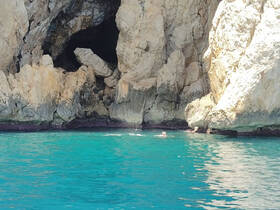 Swimmers enjoy the stunning turquoise waters near a rocky cave, showcasing the beauty of coastal adventures.
