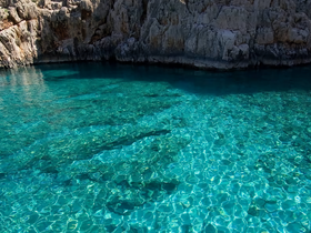 A serene view of crystal-clear waters reflecting sunlight, surrounded by rocky cliffs — a picturesque spot for boating or swimming.